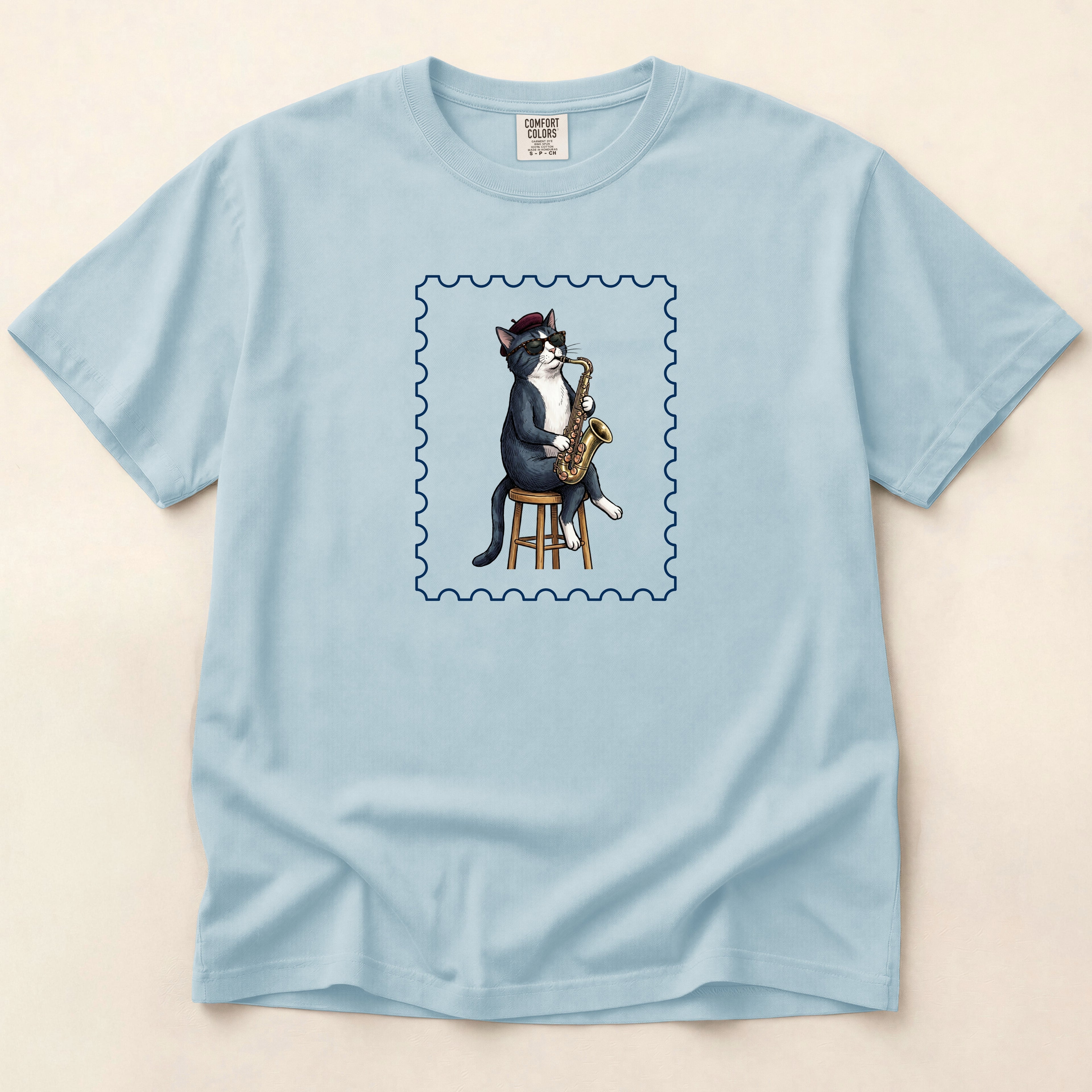 Light blue t-shirt with a cat playing saxophone design on a beige background